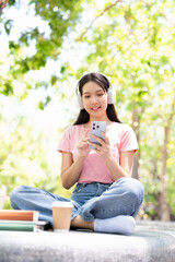 Young student woman wear casual clothes headphones sits alone outdoor  listen music use mobile cell...