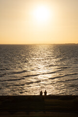 Fototapeta premium Couple watching golden sunset over calm ocean waves