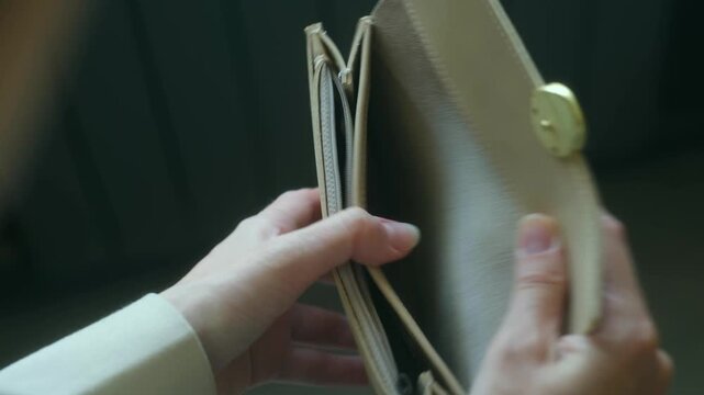 Female hands revealing empty beige wallet, signaling financial struggle and economic hardship faced by professional woman experiencing monetary challenges. Woman opening empty beige wallet