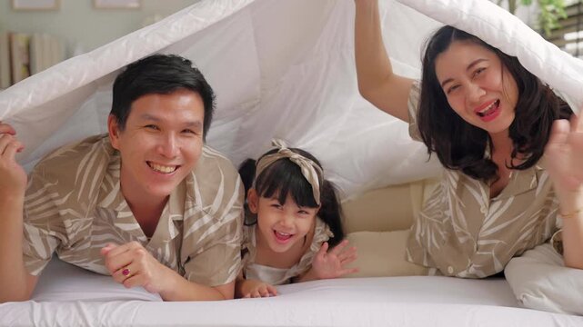 asian family bonding lifestyle Happy young family covered over head Let have fun under the blanket Family lying under bedspread asian family parent and daughter play peekaboo under blanket bedroom