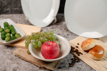 A white ceramic bowl filled with fresh, colorful fruits and vegetables. Healthy eating concept with apple, grapes, orange, and bell pepper.