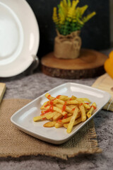 Close-up of crispy golden french fries topped with a drizzle of ketchup, served on a white rectangular plate over a burlap placemat.