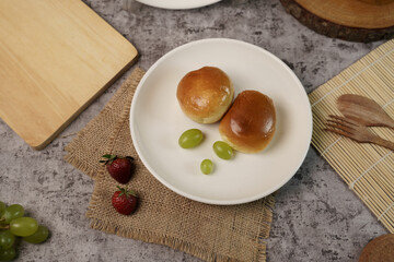 Simple breakfast flat lay with two fresh bread rolls and green grapes on a white plate, set on a rustic grey table with strawberries.