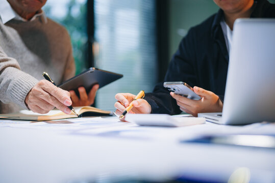 business documents on office table with tablet, smart phone and laptop and two colleagues discussing data - Powered by Adobe