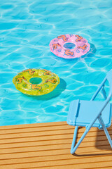 Obraz premium Summer pool with colorful inflatable rings and lounge chair on wooden deck, featuring vibrant blue water for tropical holiday and product design backdrops.