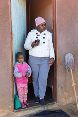 Africa village, young african woman and child standing in the door frame using a phone