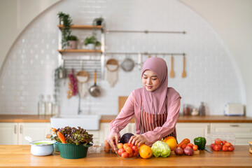Muslim woman wearing hijab preparing fresh vegetables and fruits in kitchen, healthy lifestyle...