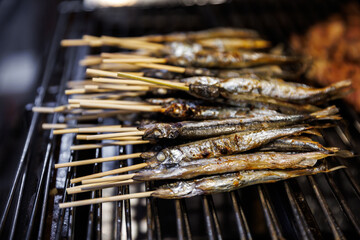 Delicious grilled Shishamo (Japanese smelt or capelin), seasoned with salt and filled with roe, being cooked on a hot barbecue grill. A popular and savory Japanese street food or snack.
