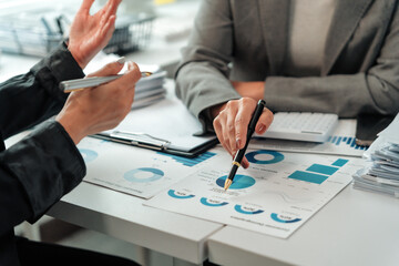 Two businesswomen are analyzing financial charts and discussing data during a productive office meeting, collaborating on important business decisions
