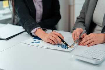 Two businesswomen collaborating in an office meeting, analyzing financial data and charts while...