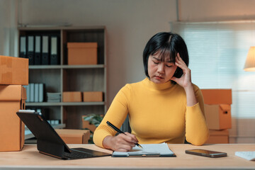 Young asian entrepreneur woman is feeling tired and stressed from working with boxes of products...