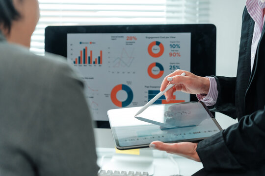Businesswomen are having a meeting and analyzing financial charts and graphs displayed on a digital tablet and computer screen, working together to improve their business strategies