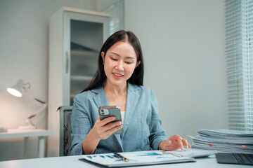Young Asian businesswoman using smartphone and working with calculator and financial documents in...