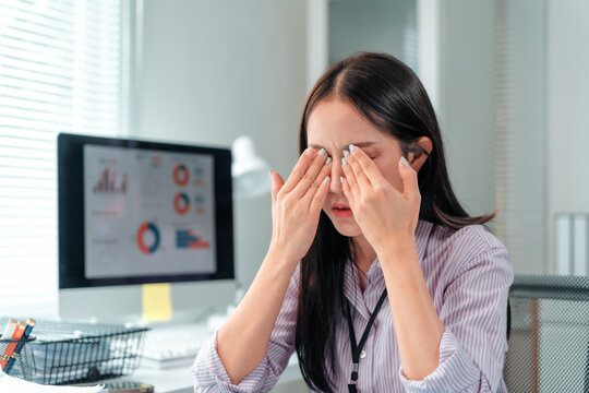 Young office worker suffering from eye strain, dry eye syndrome, bad vision, feeling eyestrain fatigue after computer work, massaging her eyes, relieving tension, taking break from work