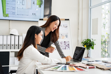 Professional young interior designers and architects working together in the office, they are using a laptop and considering material samples.