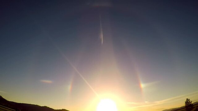 A bright sun with sun dogs and a halo above a rural landscape