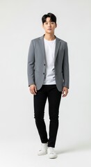 Young Korean man poses confidently in gray blazer, white t-shirt, and black pants, standing in studio with a clean white backdrop.