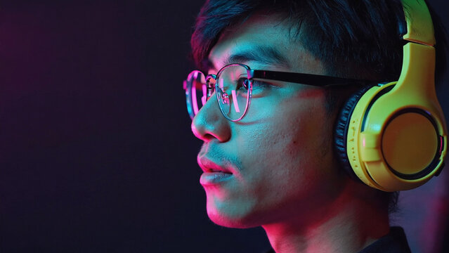 Asian adult male gamer focused wearing yellow headphones immersive virtual reality experience neon light gaming setup dark room modern technology