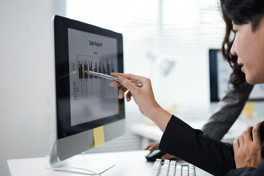 Two business professionals discussing sales reports on a computer screen, pointing at a chart, and collaborating on strategies in a modern office