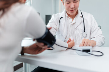 Fototapeta premium Asian doctor using a sphygmomanometer to check blood pressure of patient in hospital or clinic, emphasizing healthcare and medical practices in a professional setting