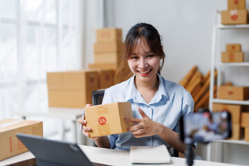 Asian woman showing a package while recording a video for her online business using a mobile phone,...