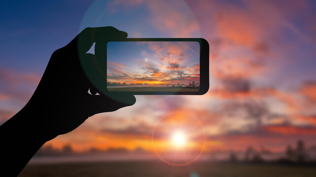 Silhouette hand holding smartphone photograph sunset