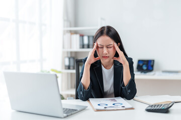 Young asian businesswoman is having headache and touching her temples while working on laptop at...