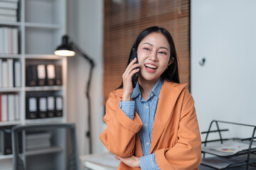 Asian businesswoman happily chatting on the phone in her office, enjoying a delightful conversation...