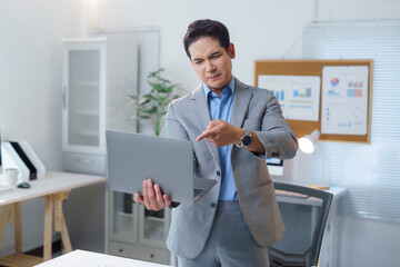 Young professional feeling stressed and disappointed with work while holding laptop and pointing at screen in modern office, expressing disapproval and concern