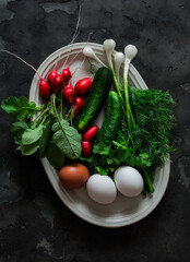 Salad ingredients - fresh cucumbers, radishes, dill, green onions, eggs on a dark background, top view