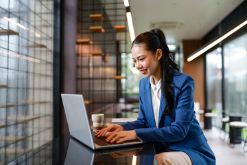 Smiling businesswoman using laptop and enjoying a matcha latte in a modern office cafe, showcasing a productive and enjoyable work environment © amnaj