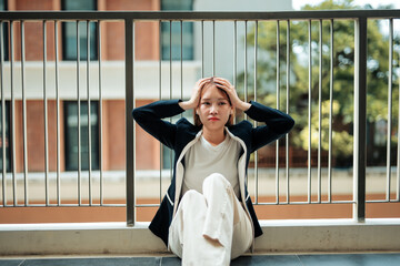 Stressed asian businesswoman is holding her head in hands while sitting on the floor of an office...