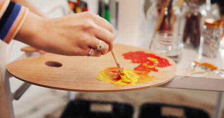 Hands, paintbrush and palette with artist in studio apartment for creative expression or inspiration. Art, mixing acrylic and painting with talented person in home for hobby, practice or skill