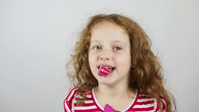 Happy little girl blows a festive pipe on a light background. Holiday birthday concept.