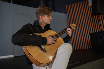 Caucasian man playing guitar while sitting on stage. 