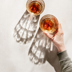 Crystal Whiskey Glasses with shadows at sunlight on beige concrete background, hand hold glass,...