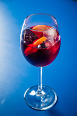 A colorful cocktail with fruits and ice is beautifully presented in a tall glass on a vivid surface