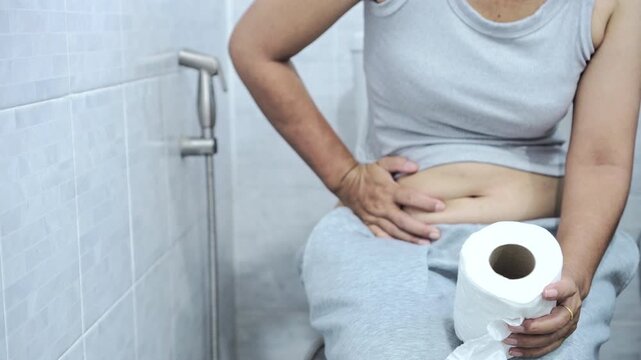 woman sitting on the toilet, struggling with hard and lumpy stools, showing signs of chronic constipation and difficulty passing bowel movements, hand holding tissue paper