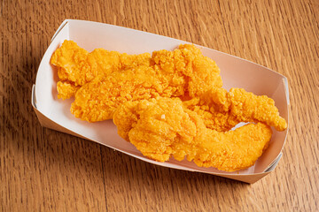 Juicy fried chicken tenders with a crispy coating displayed in a paper takeout container on wood
