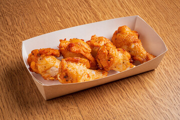 Deliciously fried chicken drumsticks arranged in a simple paper tray on a warm wooden surface