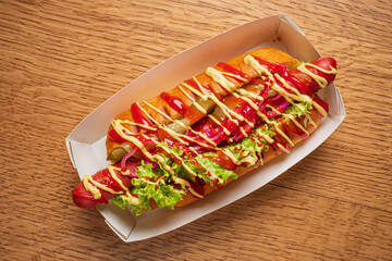 A gourmet hot dog with vibrant toppings awaits in a white tray, ready to be enjoyed