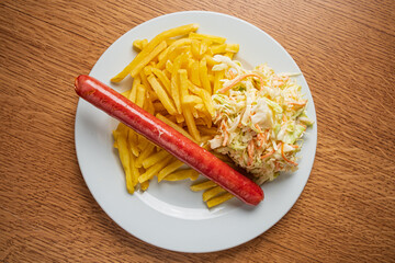 A hot dog rests beside golden fries and a serving of colorful coleslaw on a wooden table