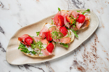 Delight in vibrant bruschetta featuring prosciutto, strawberries, and greens elegantly arranged