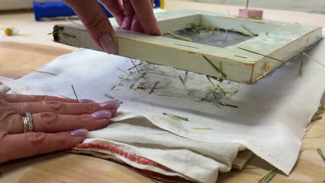 Top view of handmade floral paper on cloth, ready for drying. Final stage of eco-friendly DIY papermaking with chamomile and grass. Artistic and sustainable process