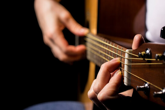 female hands playing guitar, black background. lifestyle