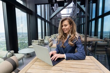 In a modern office, a focused professional woman works intently on her highperformance laptop,...