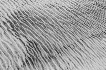 Minimalist black and white photograph of wind-sculpted sand ripples, showcasing natural textures and patterns. Perfect for abstract, nature, or background use in design and artistic projects.