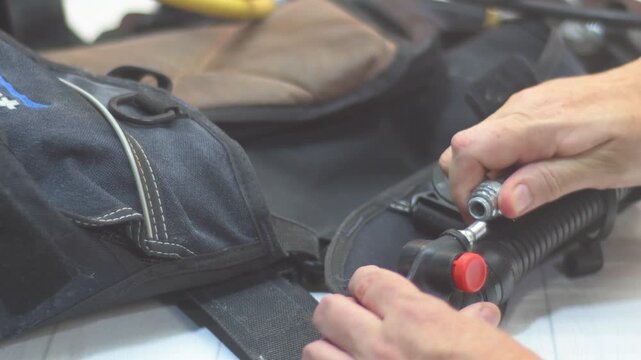 Close-up of instructor hands checking on the inflator hose on a Buoyancy Control Device, during setup, part of pre-dive scuba gear preparation.
