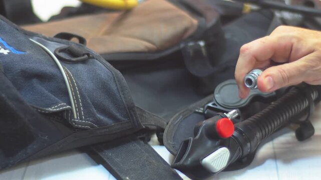 Close-up of hands connecting a scuba regulator hose to a BCD inflator valve during pre-dive equipment checks, ensuring a secure fit before diving.