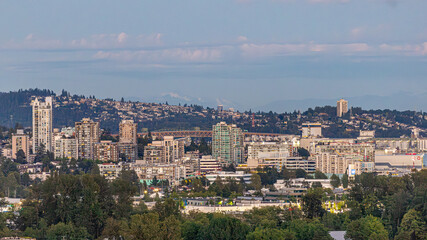 Fototapeta premium A dramatic sunset view of Vancouver's iconic downtown skyline with modern glass towers, industrial waterfront structures, and lush trees of Stanley Park across Burrard Inlet.
